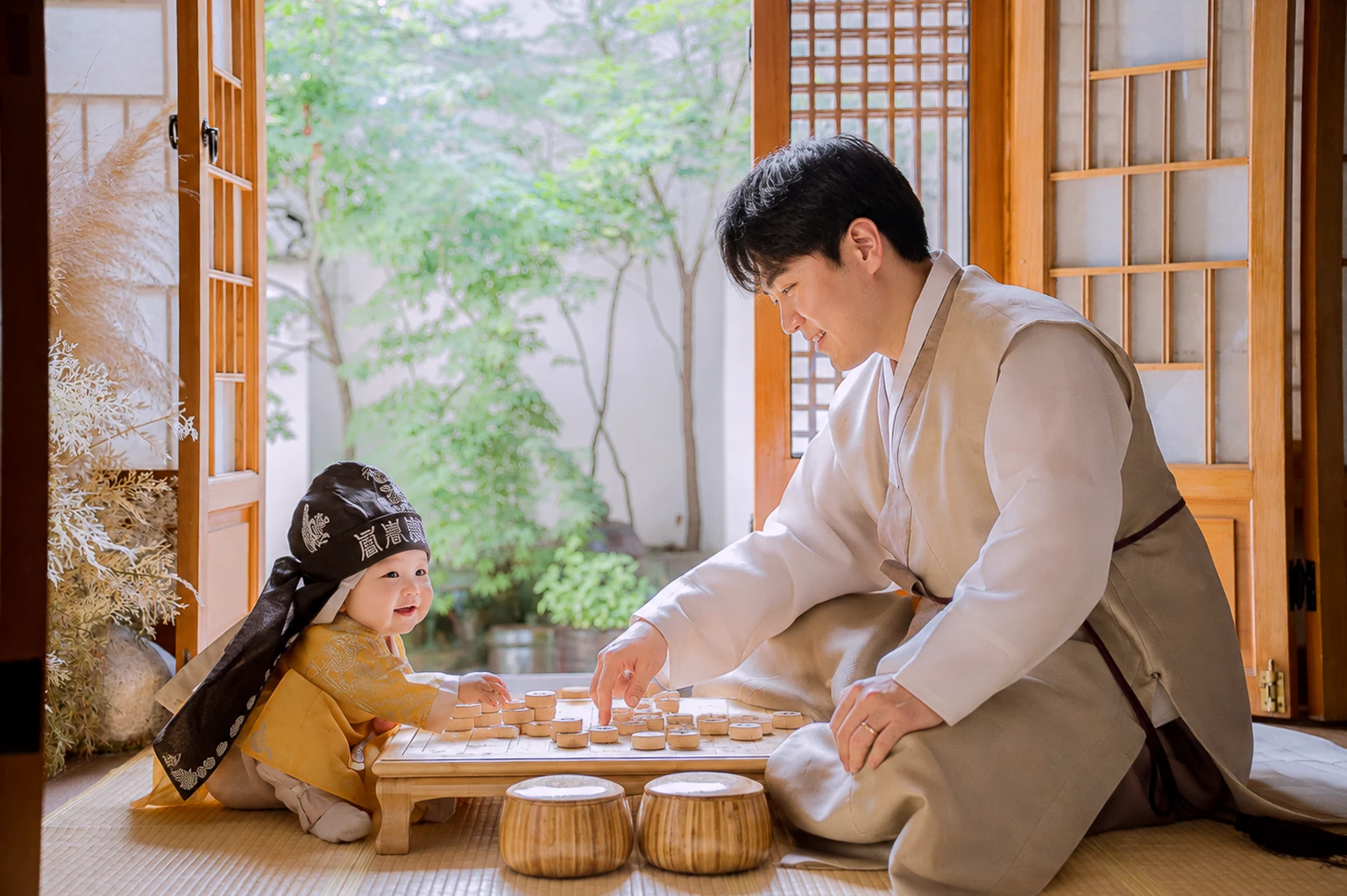 한옥 대청마루에서 한복 입은 아빠와 장기판을 사이에 두고 마주 보는 노란 한복 복건 아기 돌스냅