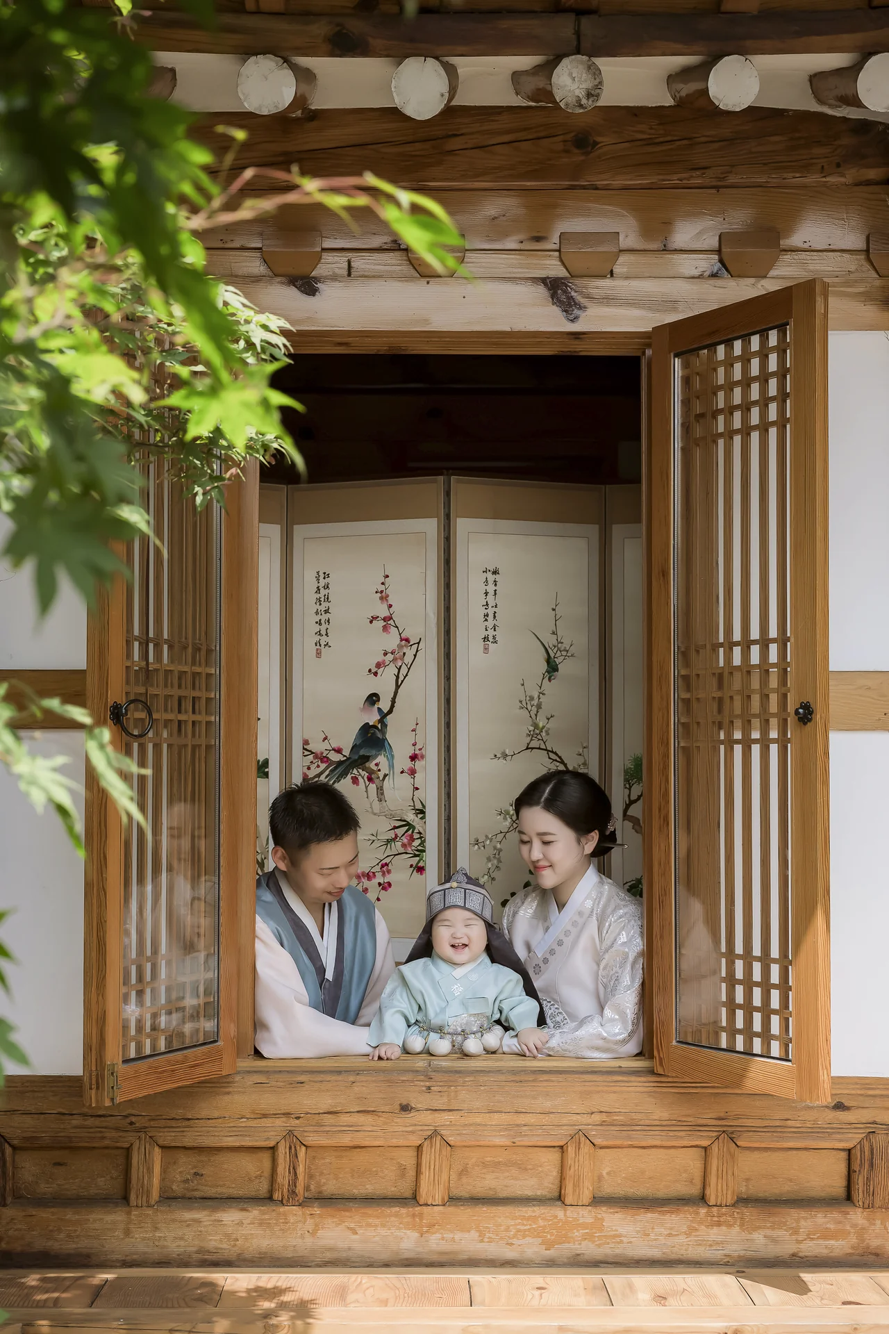 한옥 창문 프레임 속 부모와 돌복 아기의 따뜻한 가족사진