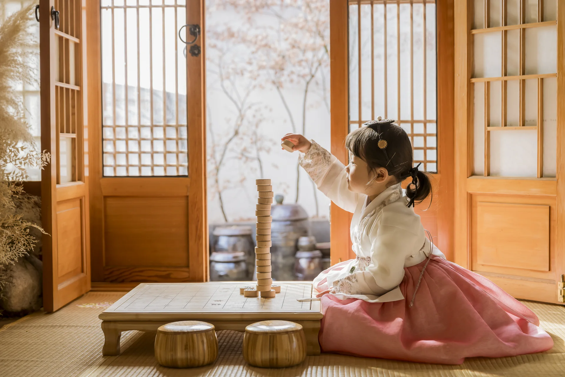 한옥 대청마루 소반 앞에서 바둑알을 쌓으며 노는 분홍 치마 한복 여자아이 돌스냅